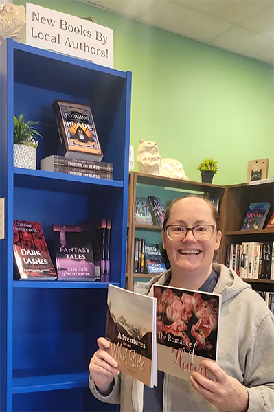 Cheryl with her books, Adventures On the Wild Side, and The Romance of Flowers posing at a blue bookshelf in a bookstore.